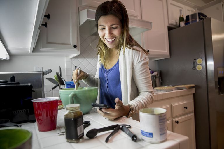 一个女人用她的iphone，因为她在厨房里做了食谱。