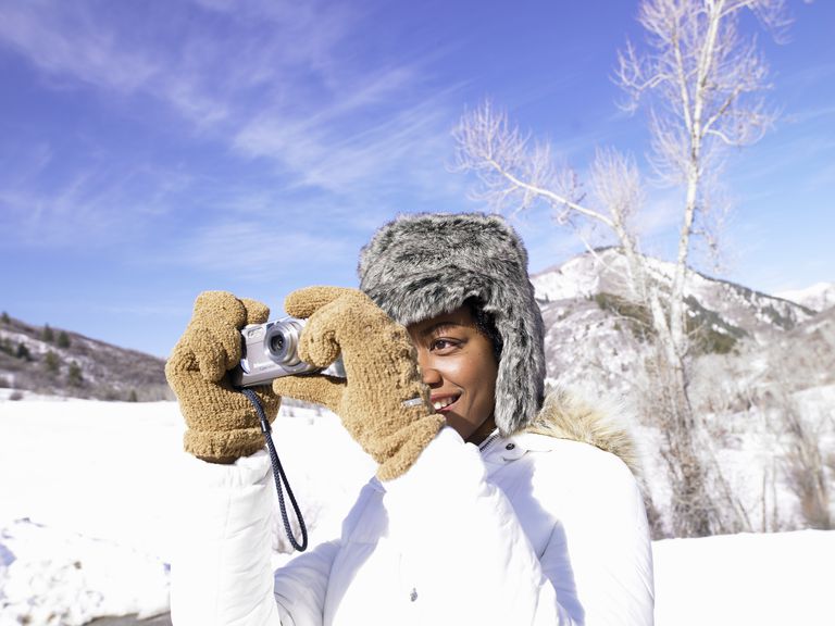 年轻女子在雪中穿着暖和的衣服用数码相机拍照