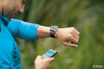 男人看着Fitbit以外在右手手腕和智能手机。